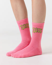 Pink socks with yellow text 'Clueless' worn by a person on a light gray background
