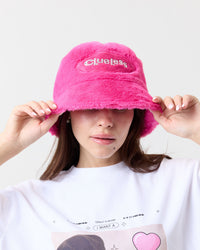 Person wearing a pink fuzzy bucket hat with 'Clueless' text, white background