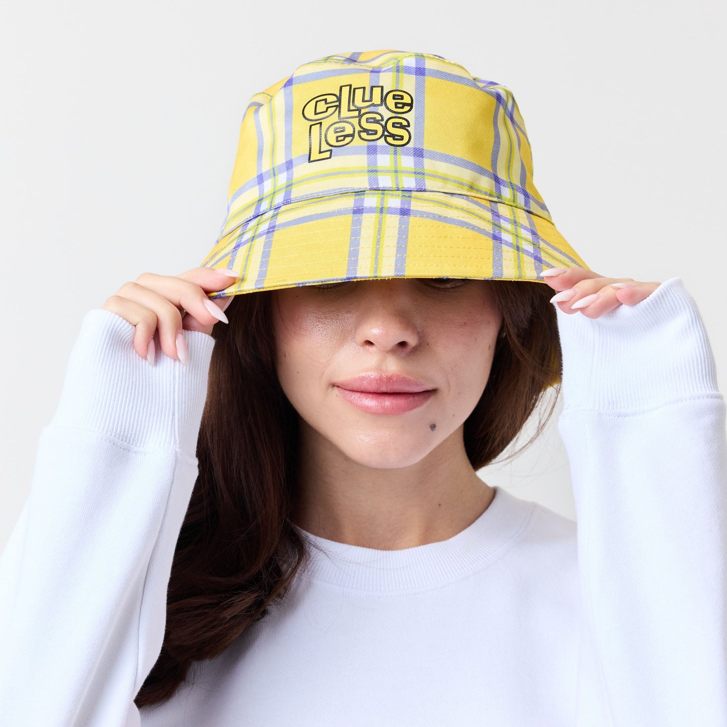 Person wearing a yellow plaid bucket hat with 'Clueless' branding on a white background