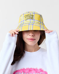 Person wearing a yellow plaid bucket hat with 'Clueless' branding on a white background