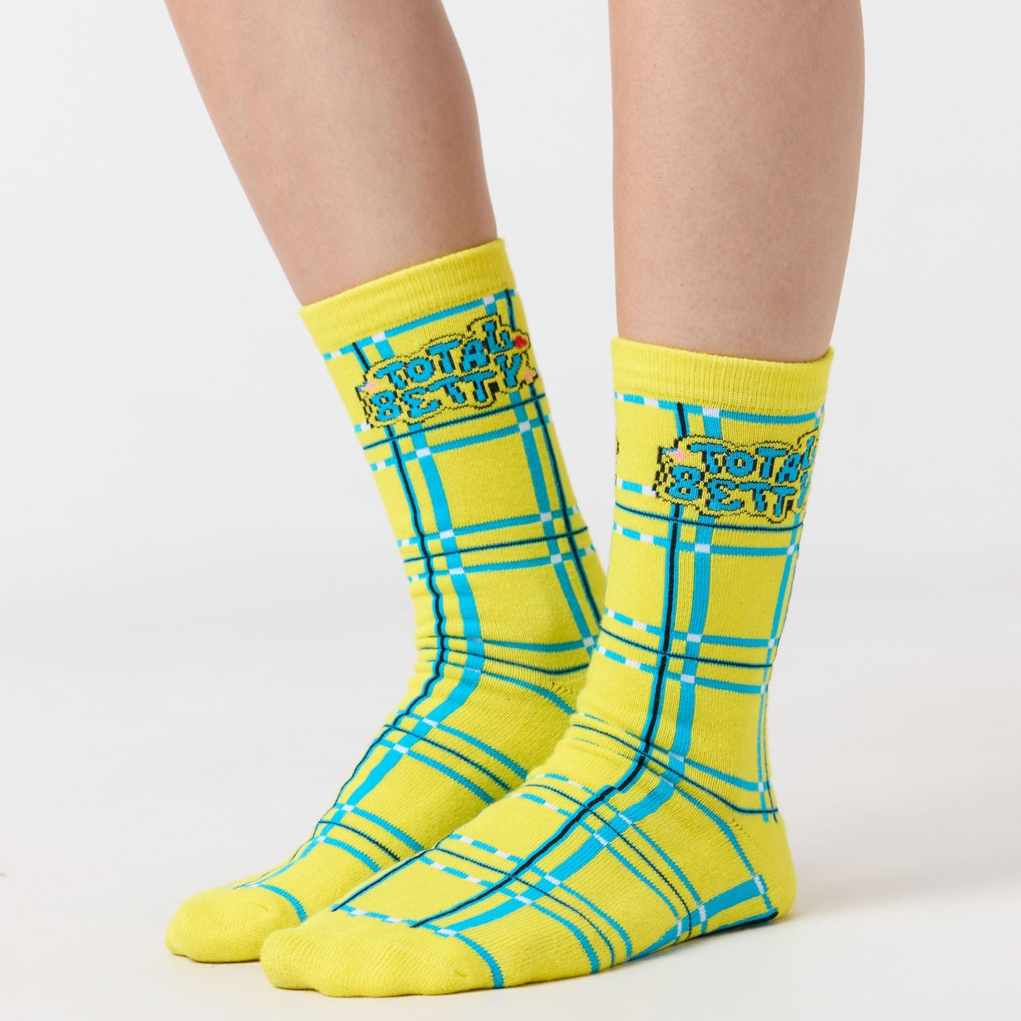 Yellow "Total Betty" Clueless checkered socks with blue accents worn by a person on a white background