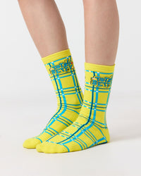 Yellow "Total Betty" Clueless checkered socks with blue accents worn by a person on a white background