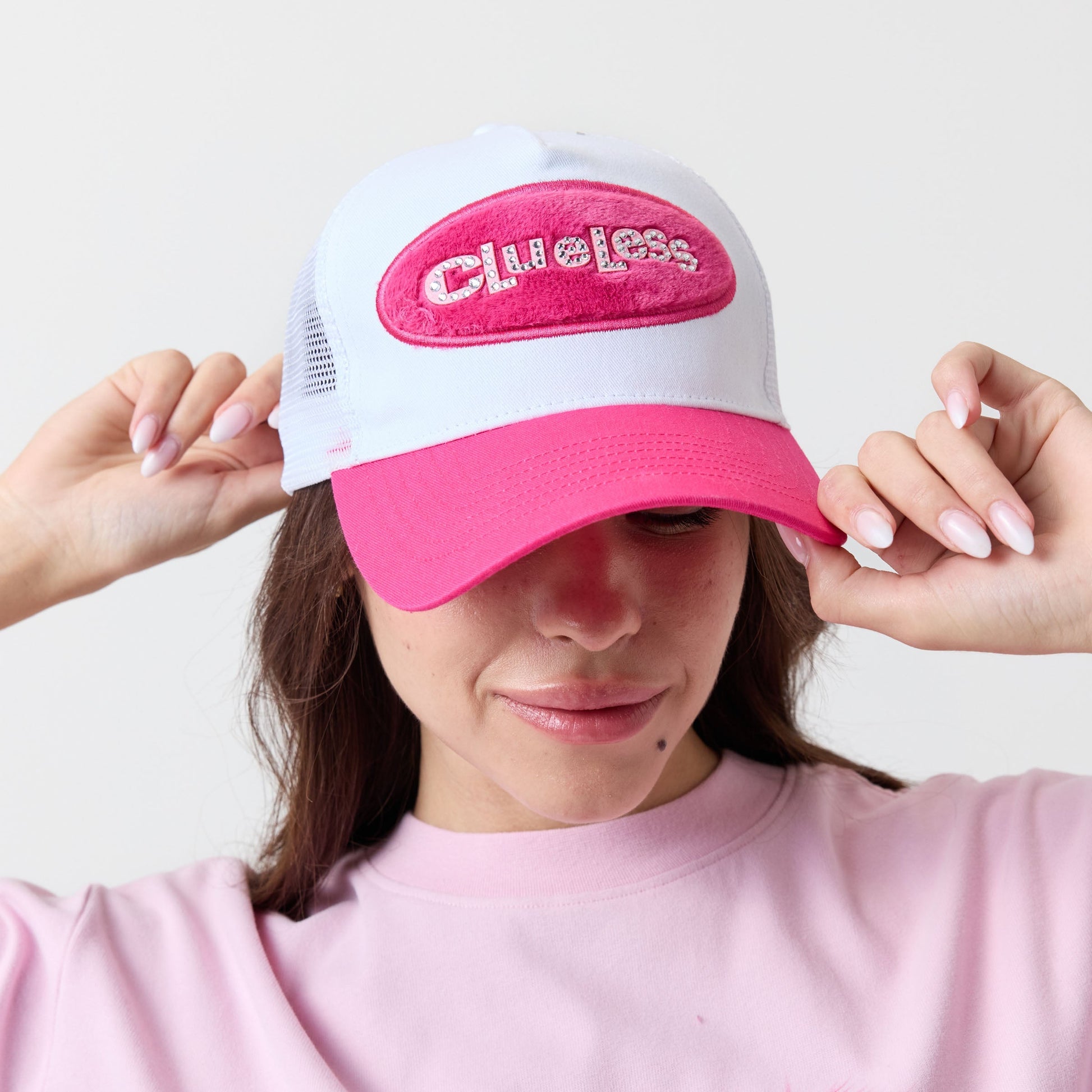 Person wearing a pink and white cap with 'Clueless' text, matching pink shirt with feather detail.