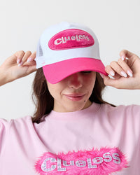 Person wearing a pink and white cap with 'Clueless' text, matching pink shirt with feather detail.