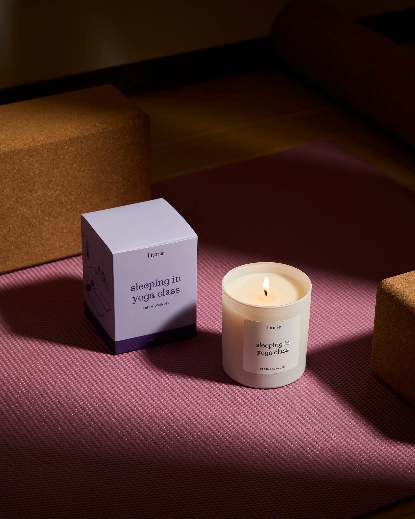 'sleeping in yoga class' candle and packaging on a pink mat with yoga blocks in the background