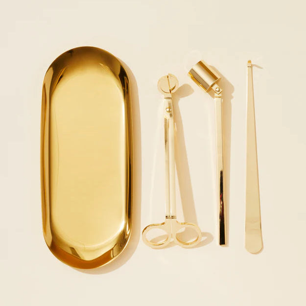 Set of gold candle tools including a tray, scissors, and tweezers on a beige background.