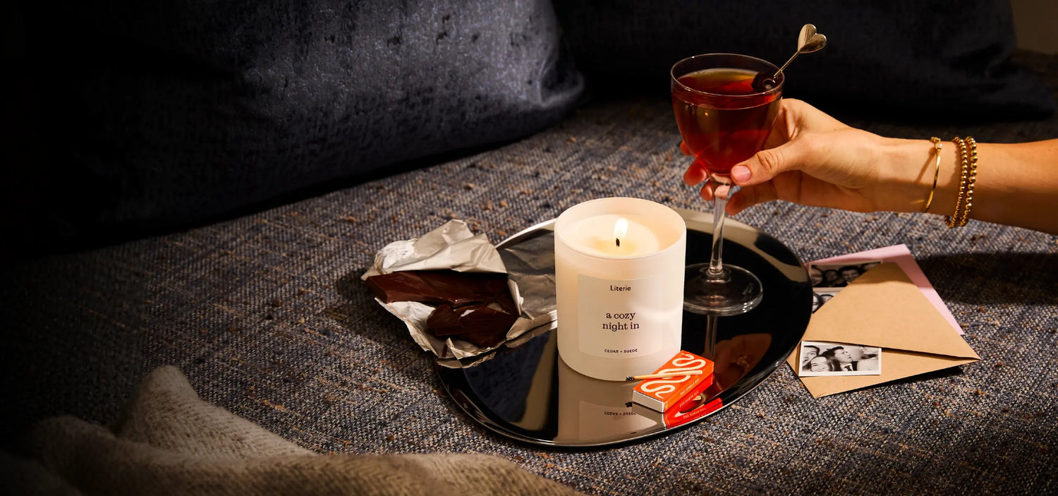 Person holding a Valentine's Day cocktail with a lit candle and chocolate on a dark surface.