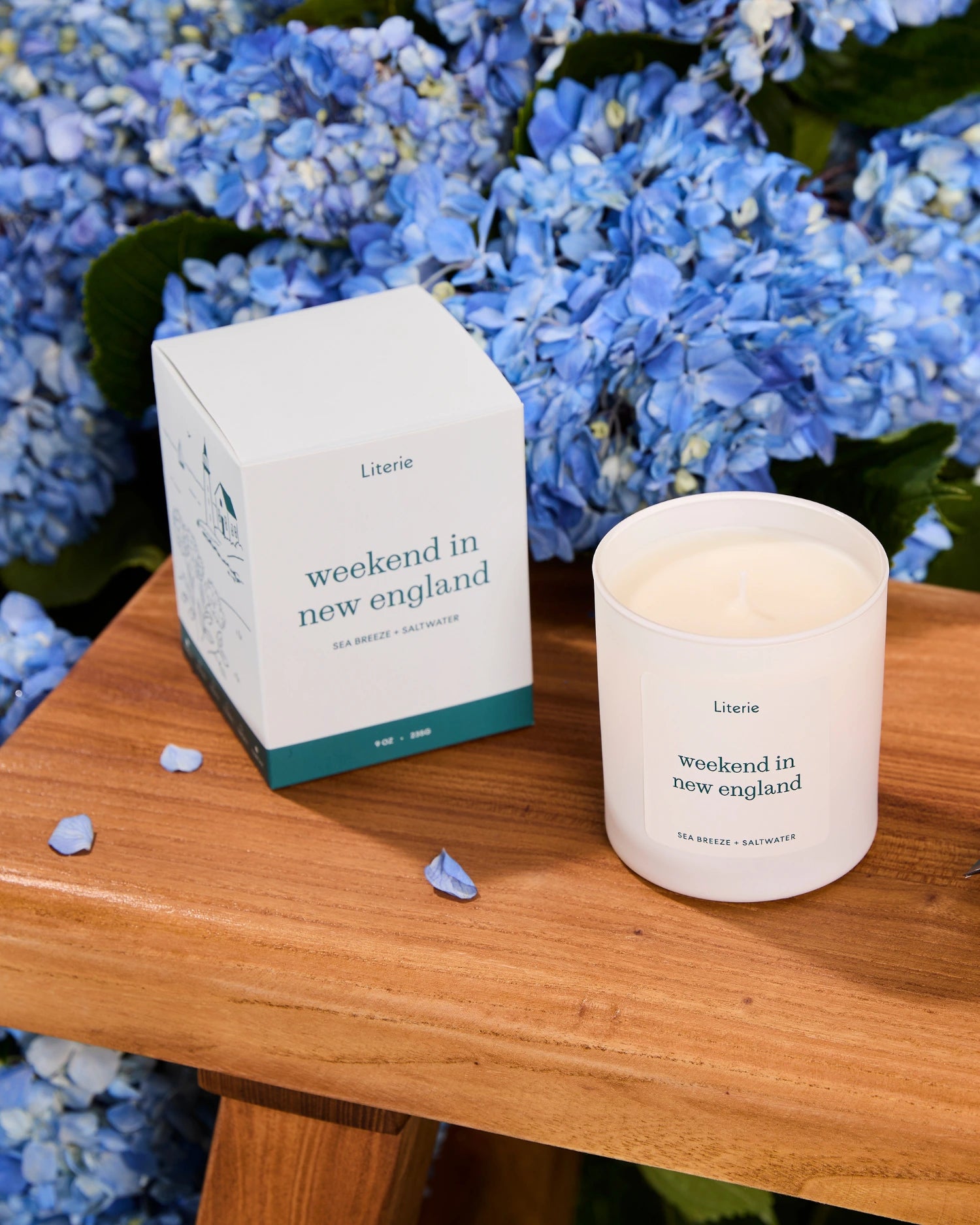 'weekend in new england' candle and packaging on a wooden surface with blue flowers in the background.