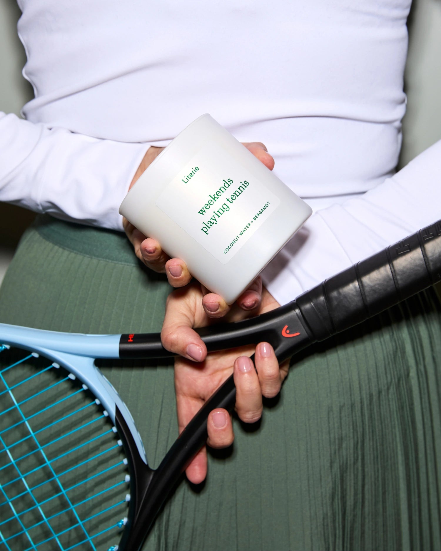Person holding a tennis racket and a 'weekends playing tennis' candle behind their back.
