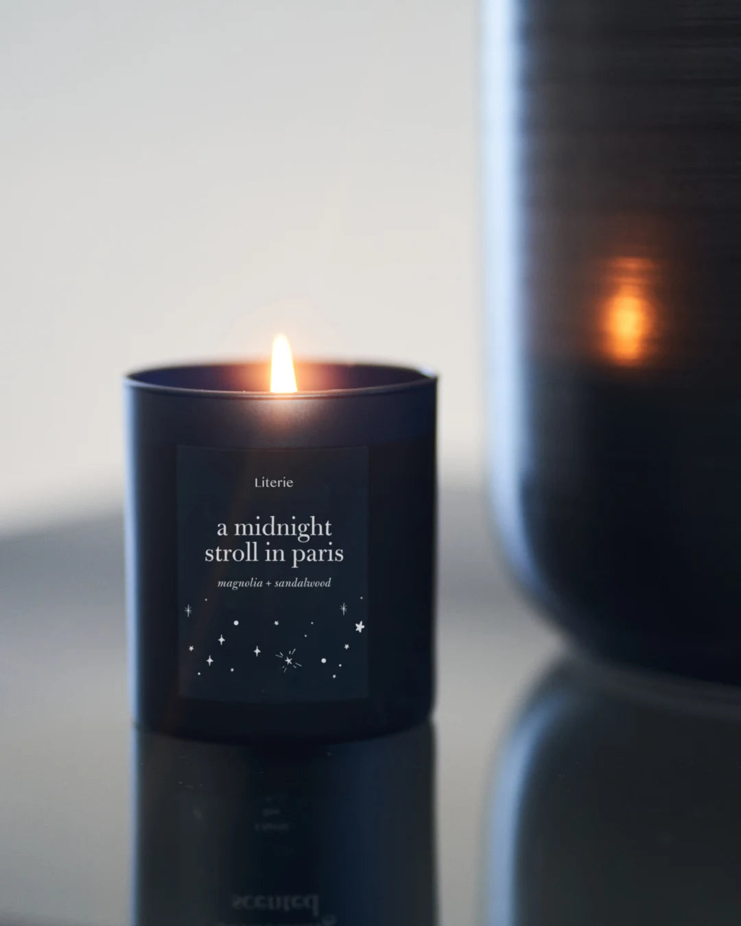 'a midnight stroll in paris' candle in aby jar on a reflective table.