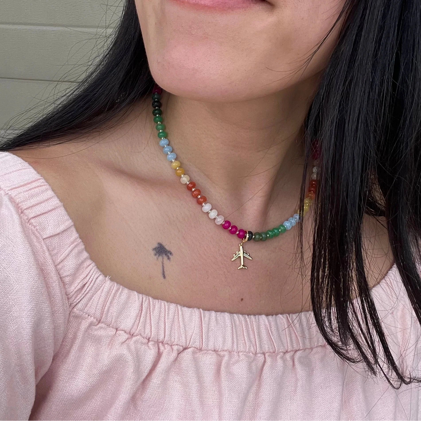 Close-up of a person wearing a colorful beaded necklace with a small airplane charm.