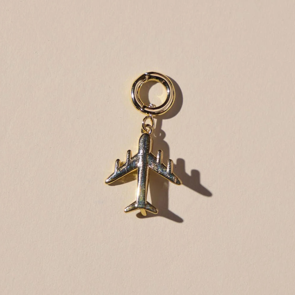 Gold airplane charm on a beige background