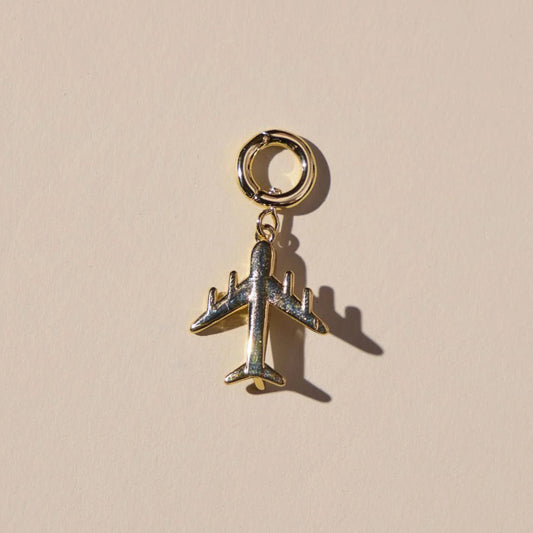 Gold airplane charm on a beige background