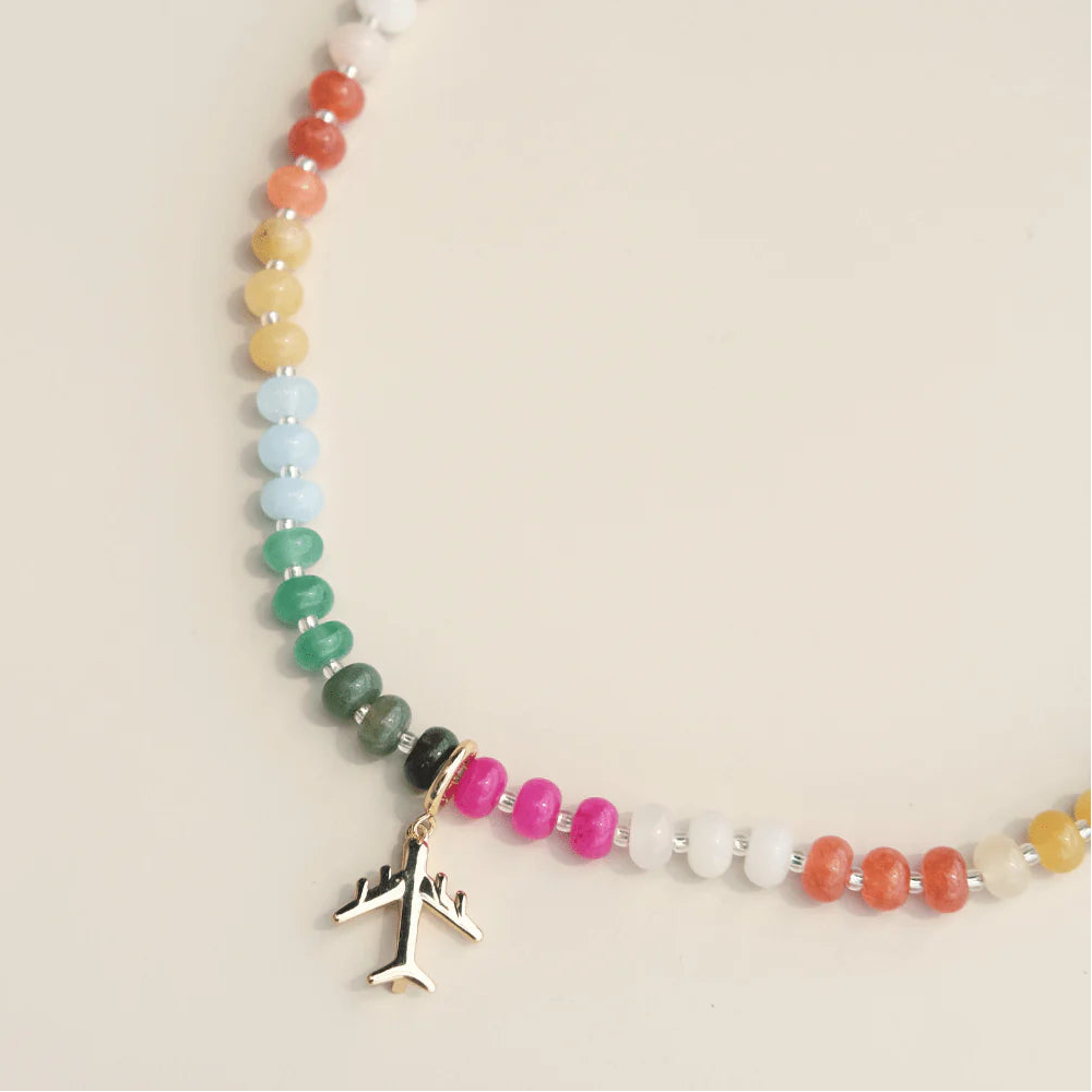 Necklace with colorful beads and airplane charm on a beige background