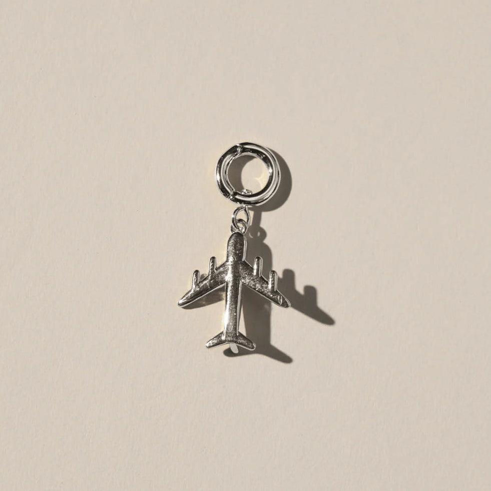 Silver airplane charm on a beige background.