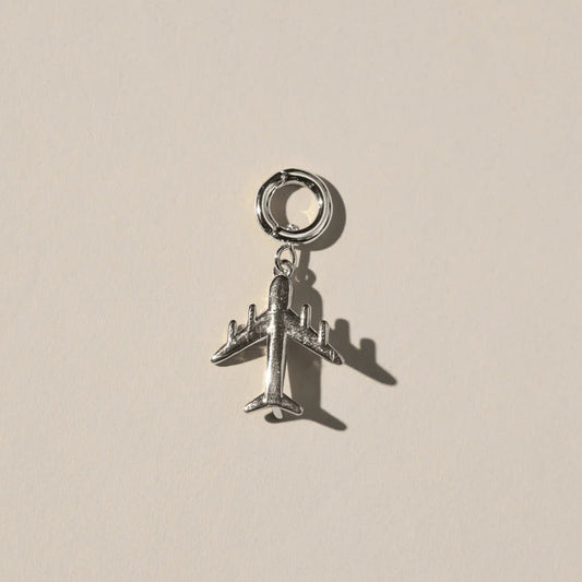 Silver airplane charm on a beige background.