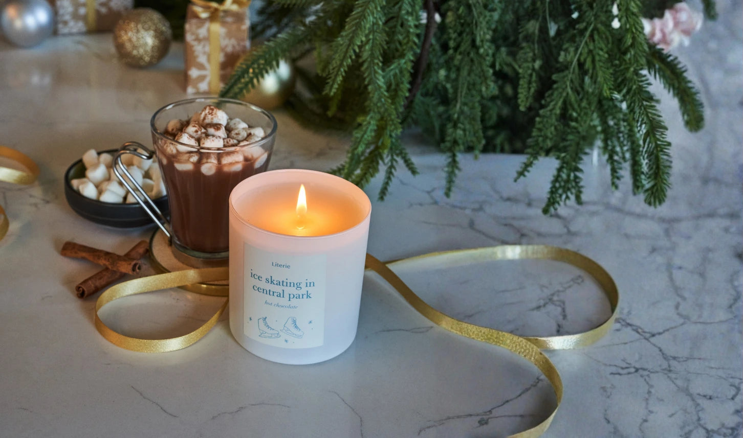 Candle with a decorative ribbon on a marble surface with a Christmas tree in the background