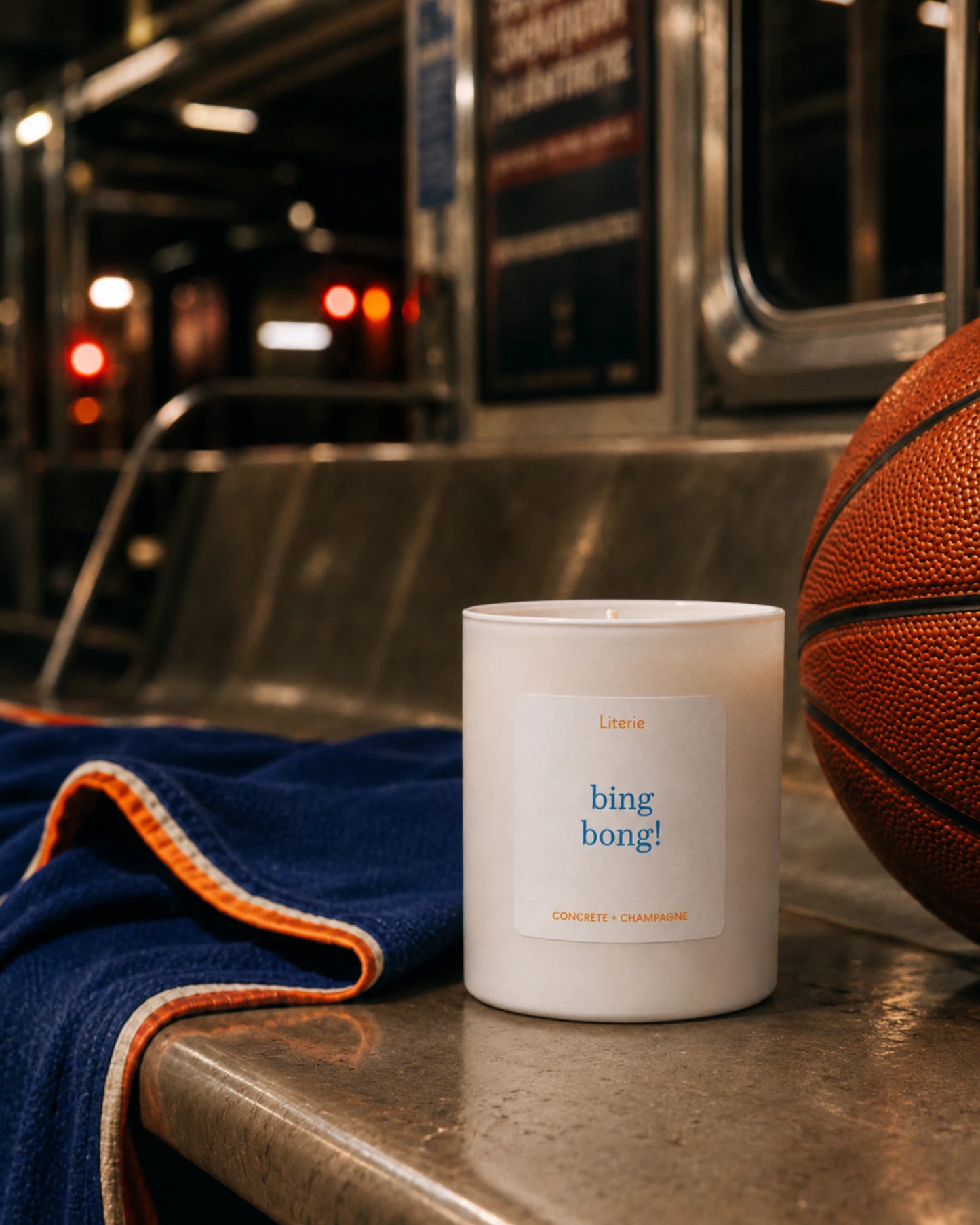 Candle labeled 'bing bong!' on a metallic surface with a basketball and blue towel in the background.