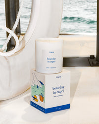 Candle and packaging with 'boat day in capri' text on a boat deck.