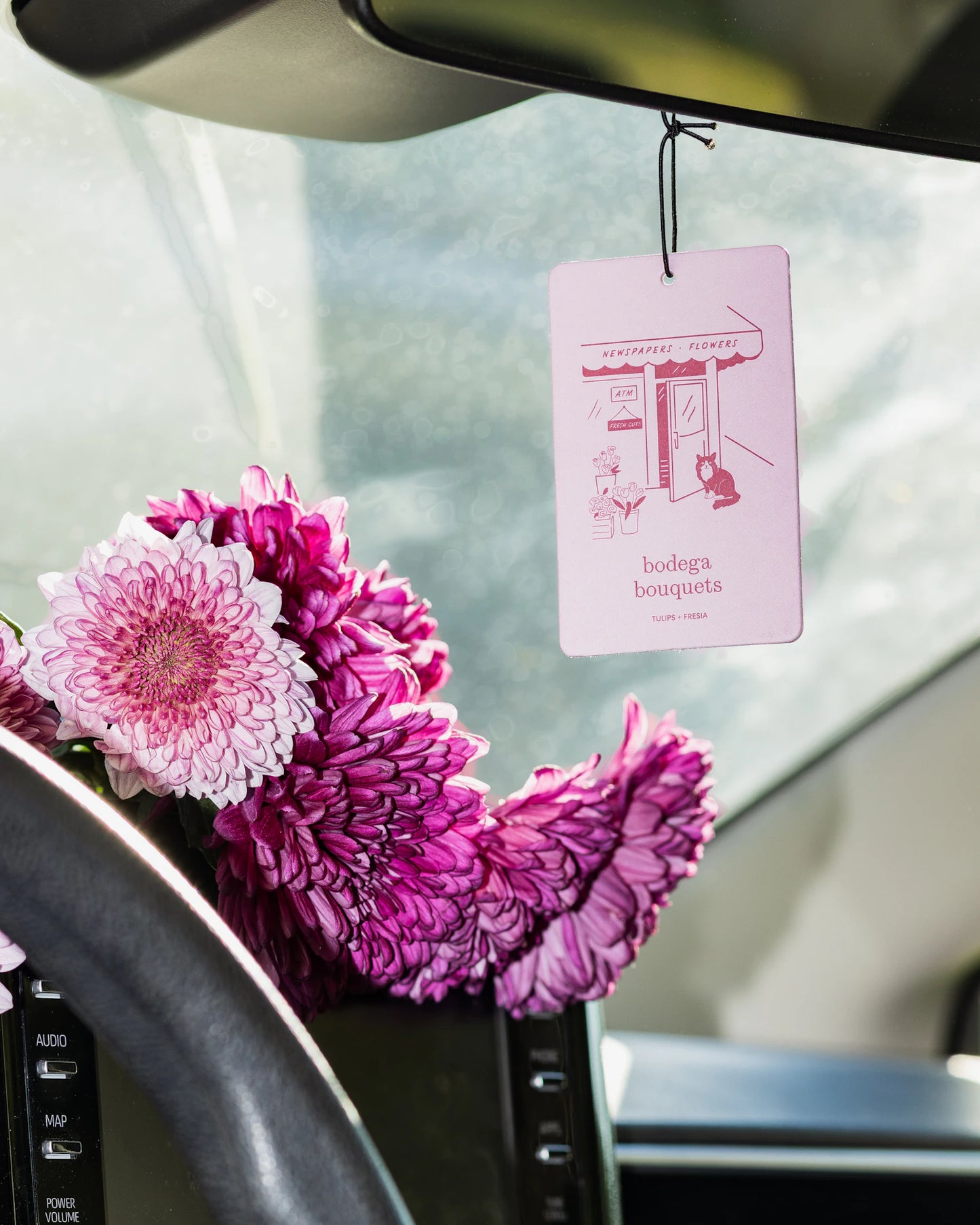 Pink flowers in a car with a hanging air freshener card.