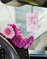 Pink flowers in a car with a hanging air freshener card.