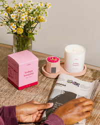 'bodega bouquets' candle and box siting on the pink candle tray next to the pink match holder with matches with flowers next to them.