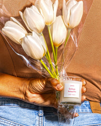 Person holing "Bodega Bouquets" little candle and tulips behind their back.