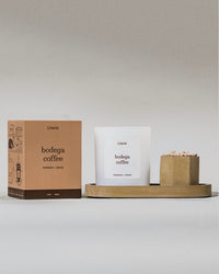 Bodega coffee candle and packaging with taupe candle tray and matches on a gray surface.