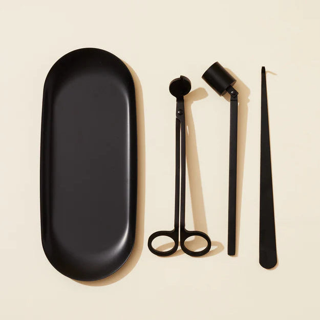 Set of black candle tools including a tray and scissors on a beige background