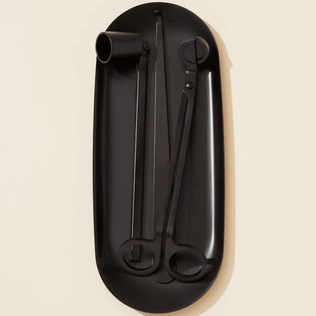 Set of matte black candle tools including a tray, scissors, and tweezers on a beige background.