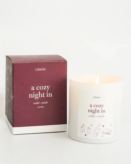 Lit candle and packaging with 'a cozy night in' text on a white background