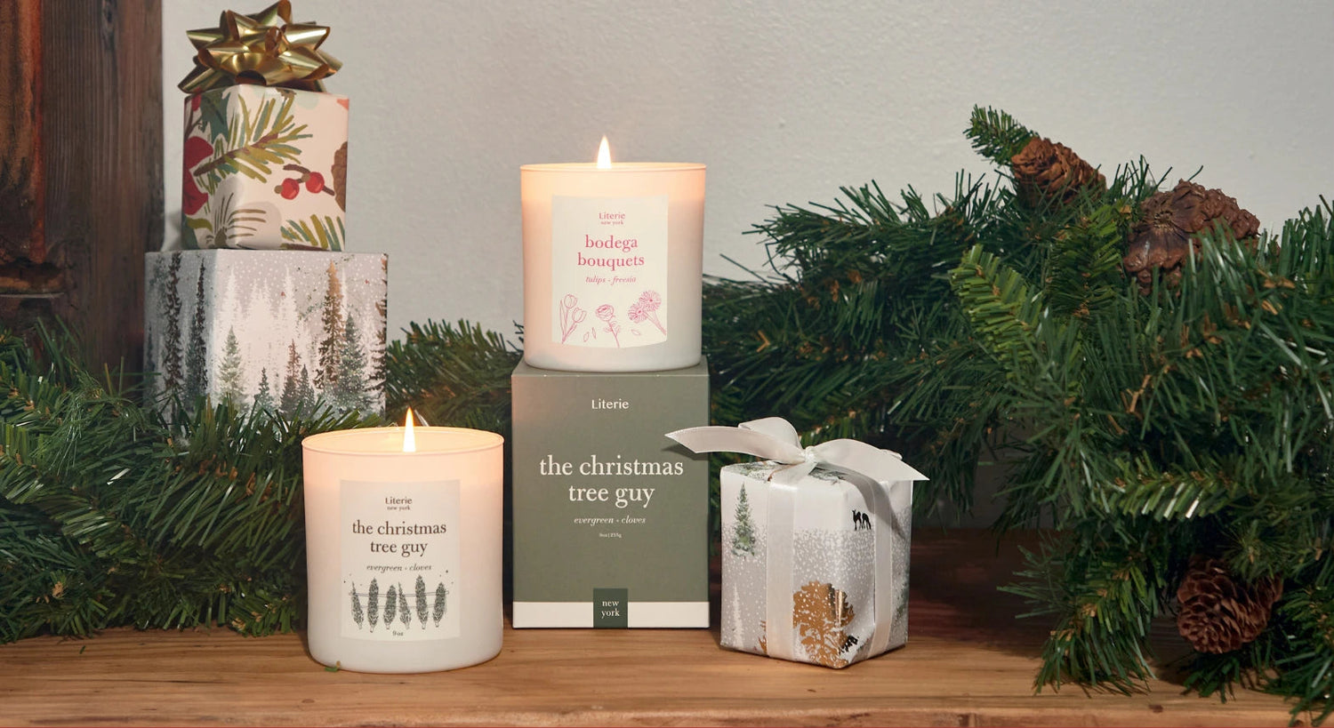 Candles and gift boxes on a wooden surface with greenery and a red border.