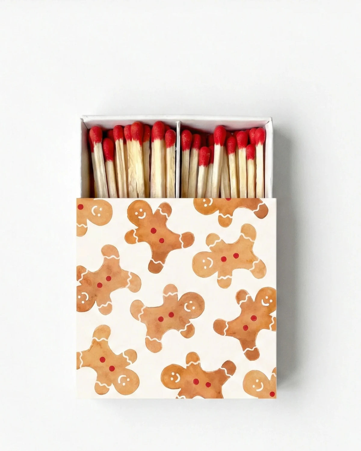 A matchbox filled with wooden matches topped with red tips, shown from above on a light gray background. The box lid has a white base printed with a repeating pattern of gingerbread cookies in warm brown tones.