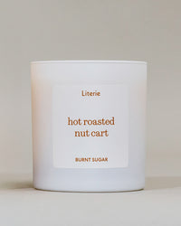 A white candle jar with a minimalist white label featuring the scent name 'hot roasted nut cart' and brand 'Literie' in a warm brown color, set against a neutral beige background.