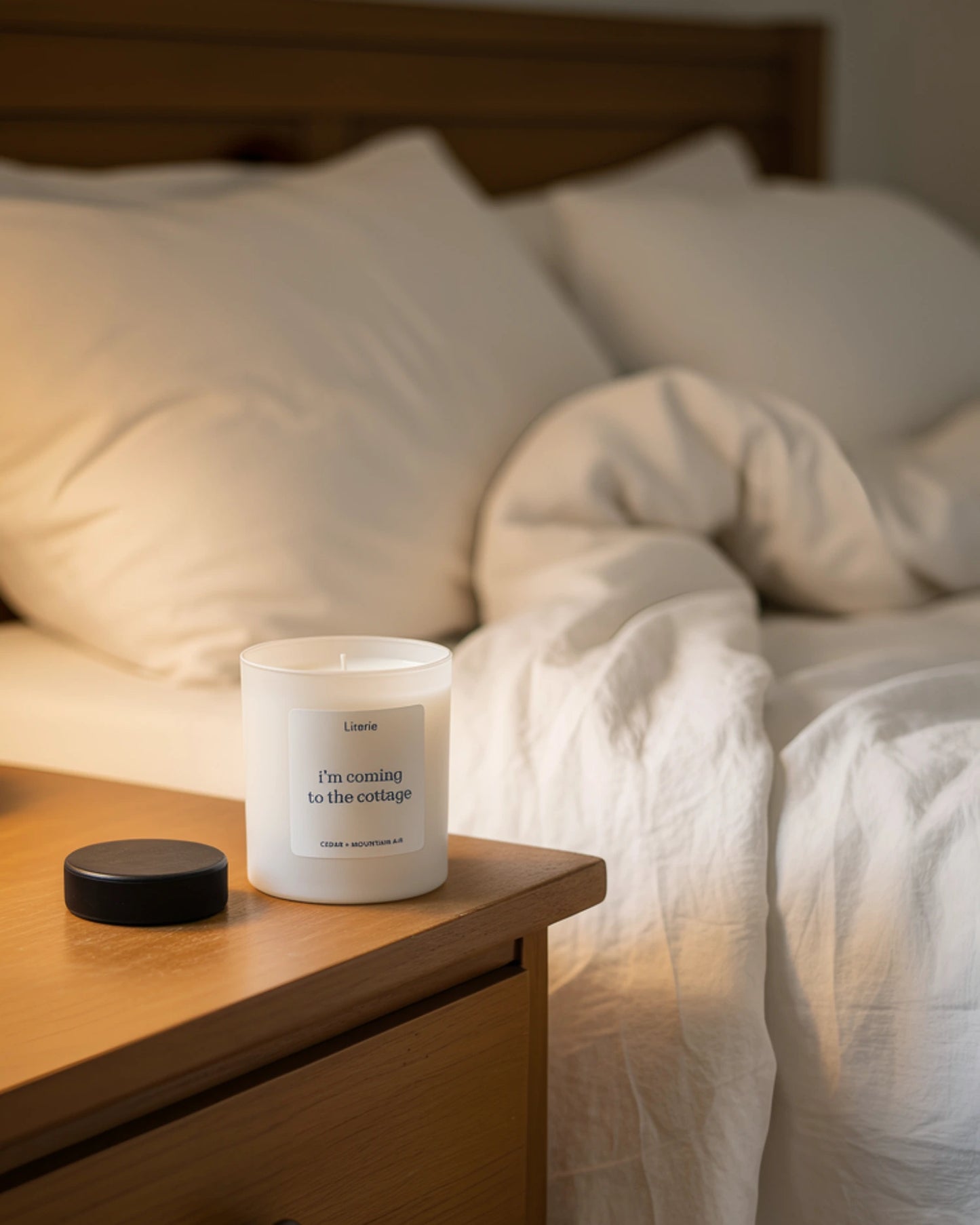 Heated Rivalry inspired candle called "I'm coming to the cottage" on a bedside table with a bed in the background