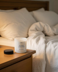 Heated Rivalry inspired candle called "I'm coming to the cottage" on a bedside table with a bed in the background