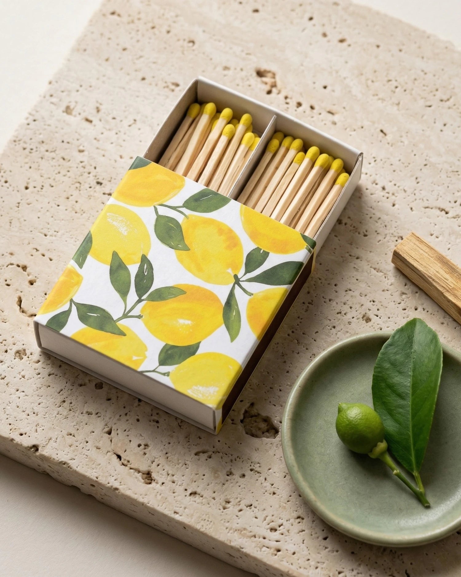 Matches with lemon patterned box on a stone surface with a green plate and leaves.