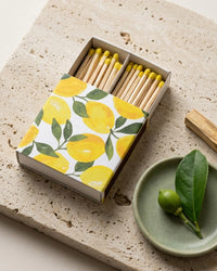 Matches with lemon patterned box on a stone surface with a green plate and leaves.