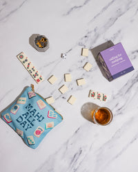 Marble surface with a blue 'mahj all day' pouch, dice, and a candle labeled 'calling for mahjong'.
