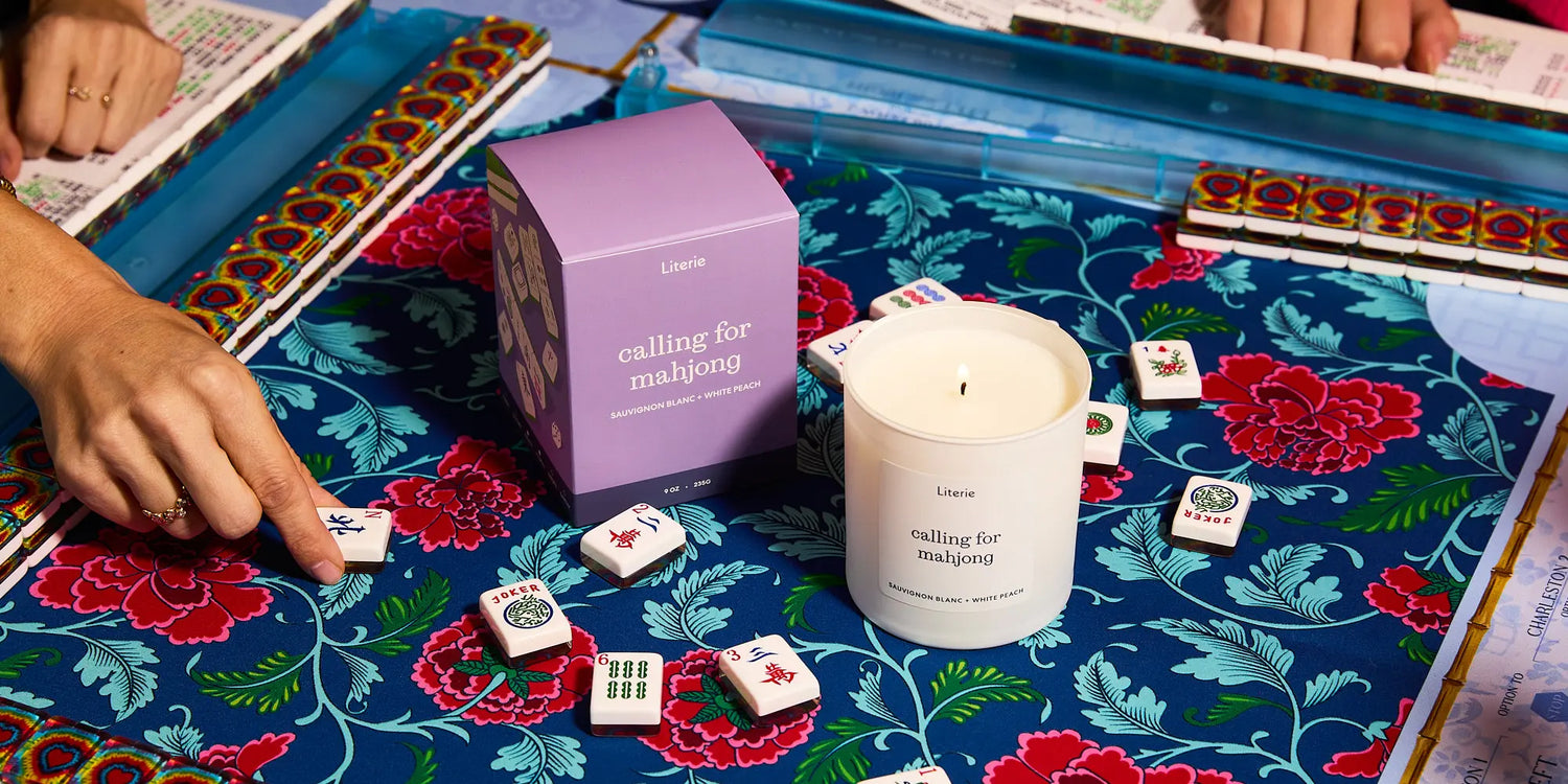 Mahjong candle and packaging on a floral mahjong mat with tiles.