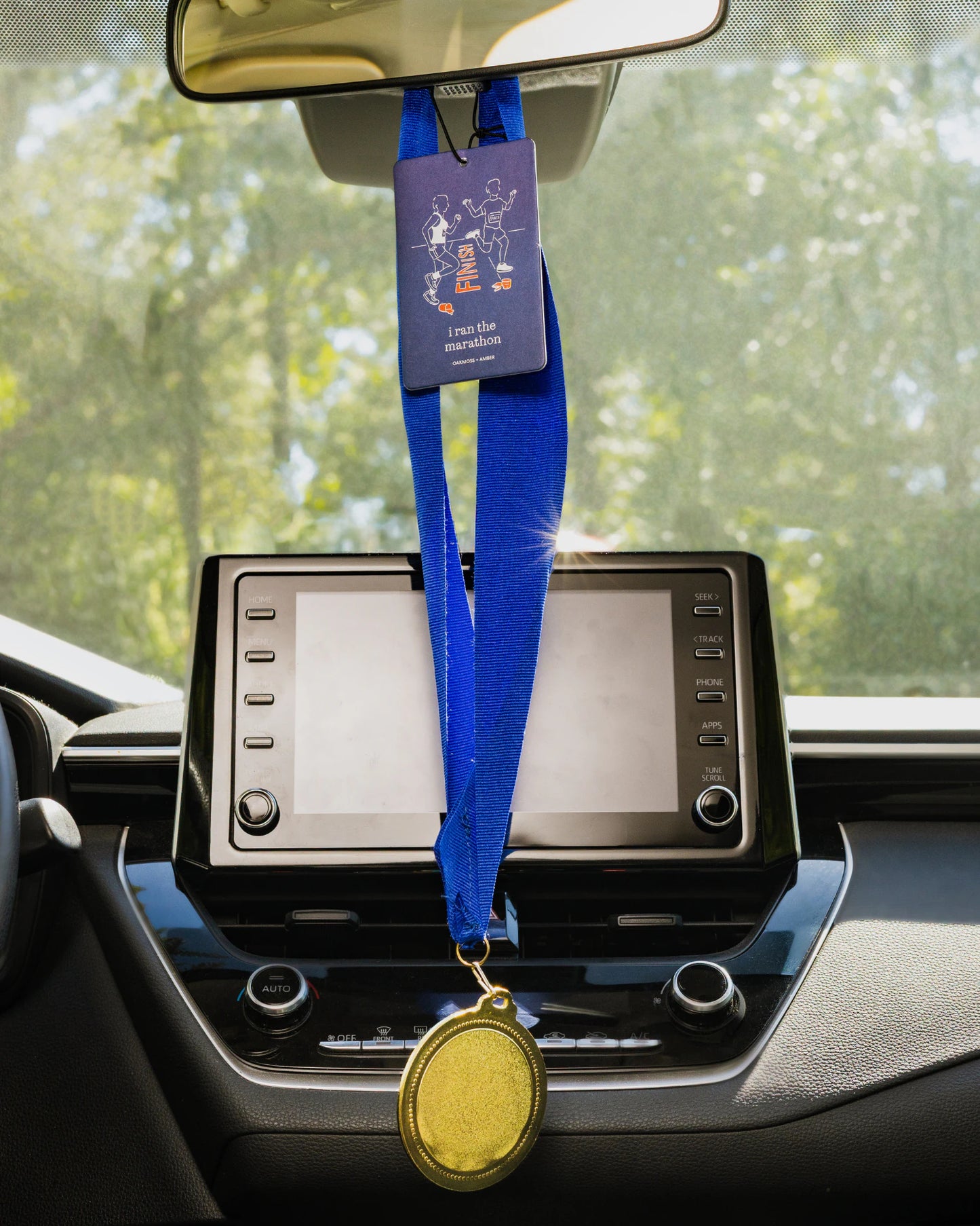 Car dashboard with a medal and marathon air freshener hanging from the rearview mirror.