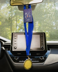 Car dashboard with a medal and marathon air freshener hanging from the rearview mirror.