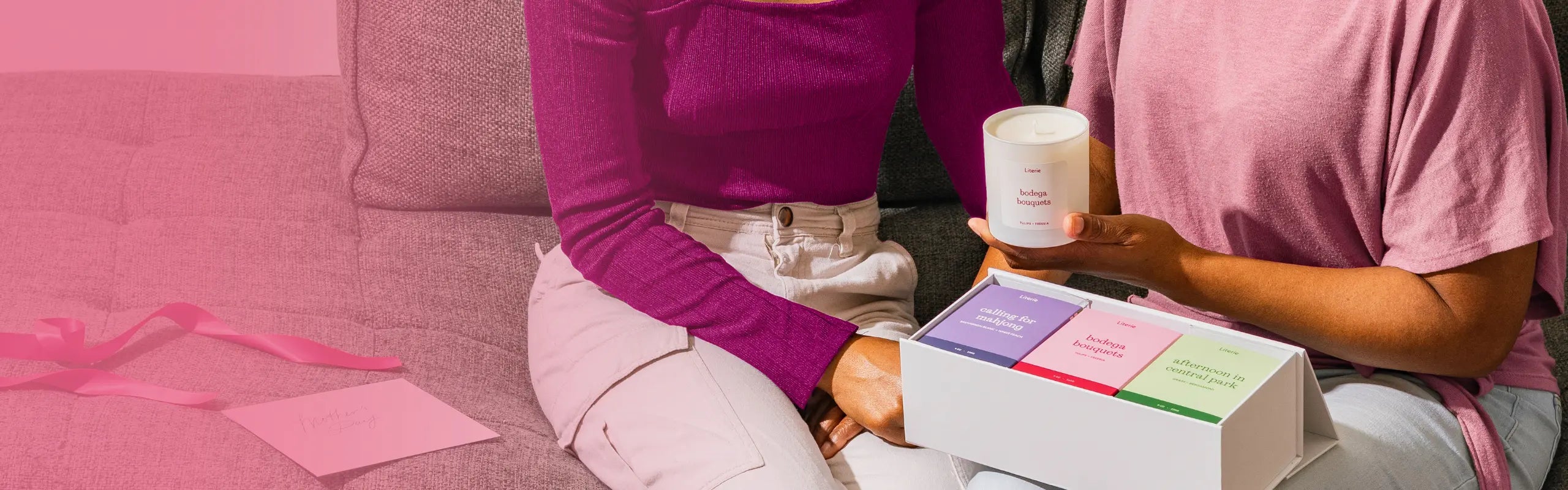Two people sitting on a pink couch with a box of candles.