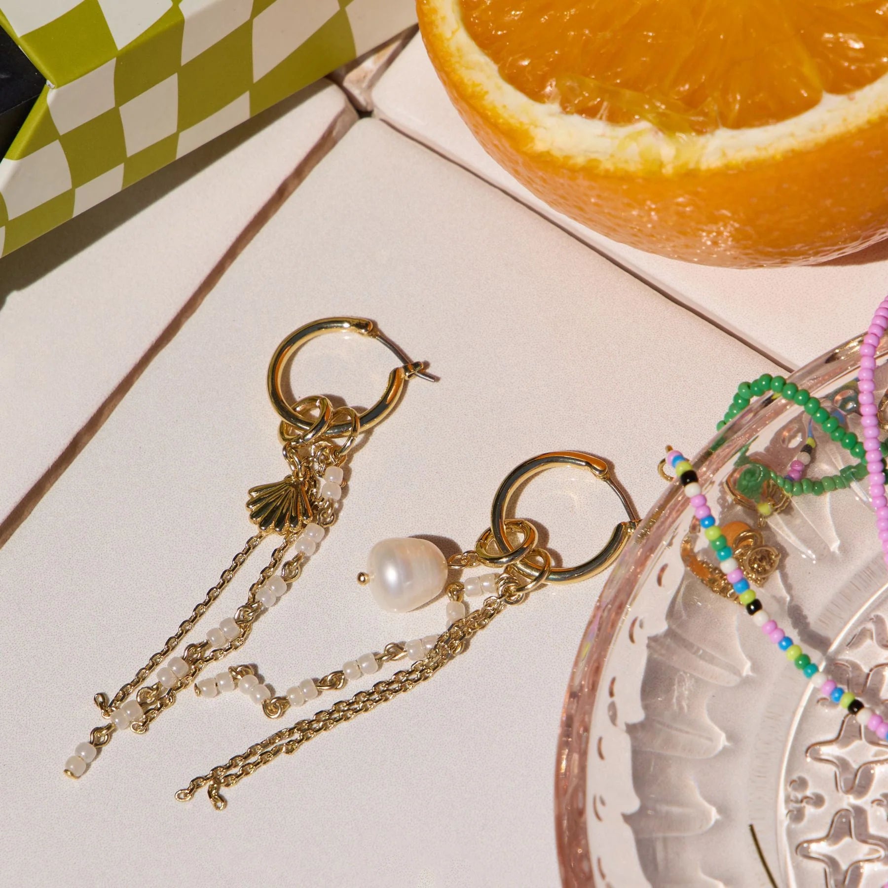 Real pearl charm styled with earrings and an orange in the background.