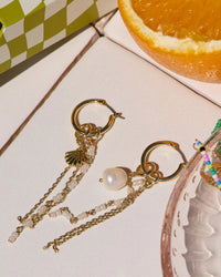 Real pearl charm styled with earrings and an orange in the background.