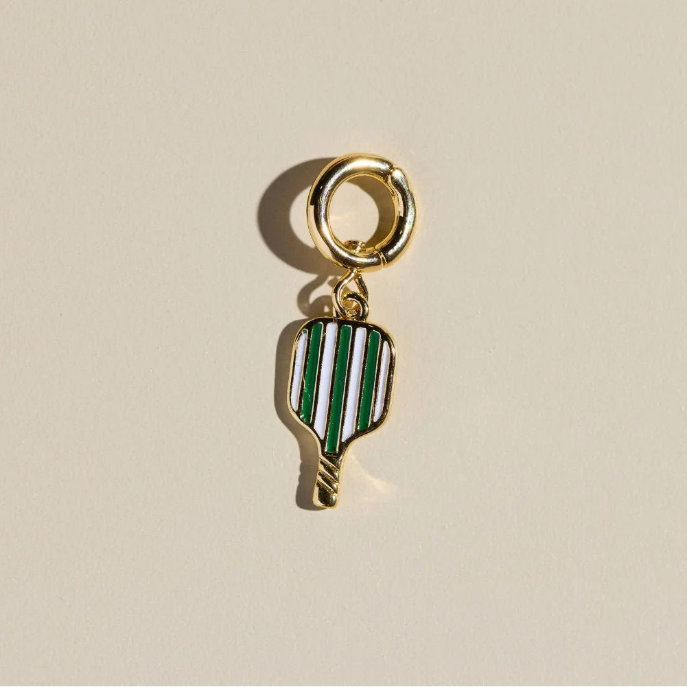 Gold pickleball charm with green and white striped design on a beige background.