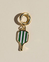 Gold pickleball charm with green and white striped design on a beige background.