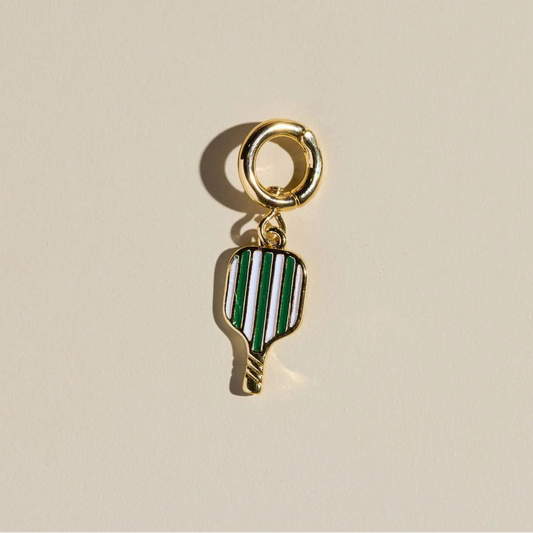 Gold pickleball charm with green and white striped design on a beige background.
