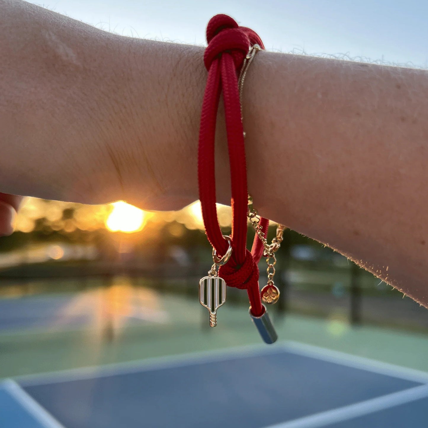 Red bracelet with pickleball charm on a wrist against a blurred outdoor background.