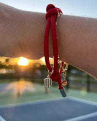 Red bracelet with pickleball charm on a wrist against a blurred outdoor background.